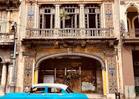 Classic blue vintage car driving past a historic colonial building in Havana, Cuba.