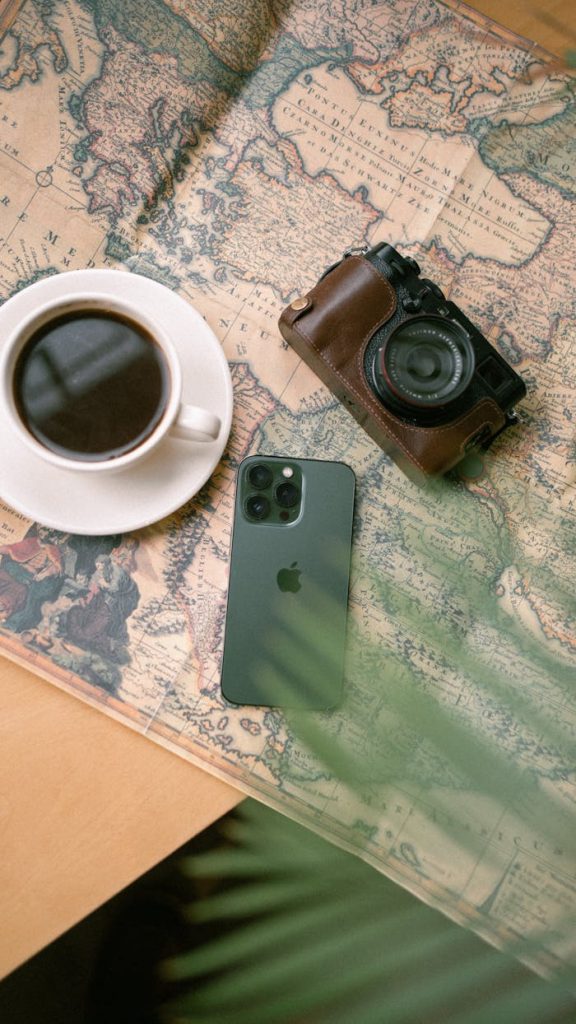 Flat lay of a coffee cup, vintage camera, and smartphone on a world map, evoking travel vibes.