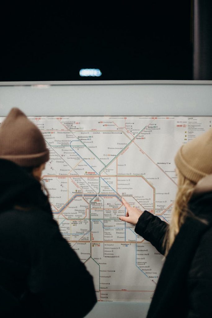 Two people in warm clothing navigate a subway map on a station platform at night.