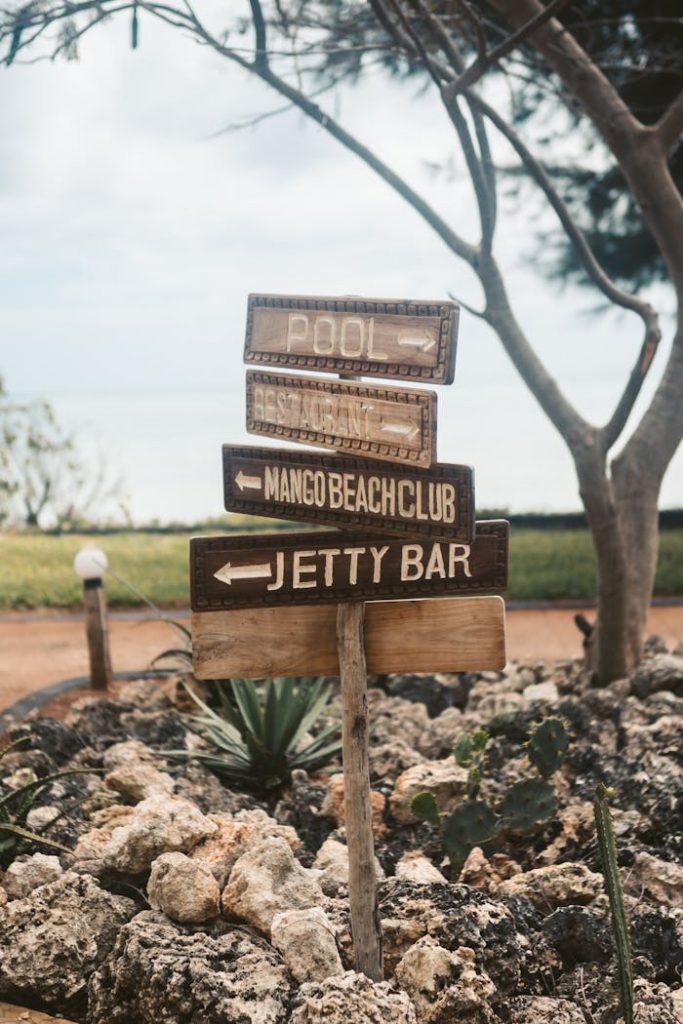 Rustic wooden signpost in a tropical setting pointing to pool, mango beach club, and jetty bar.