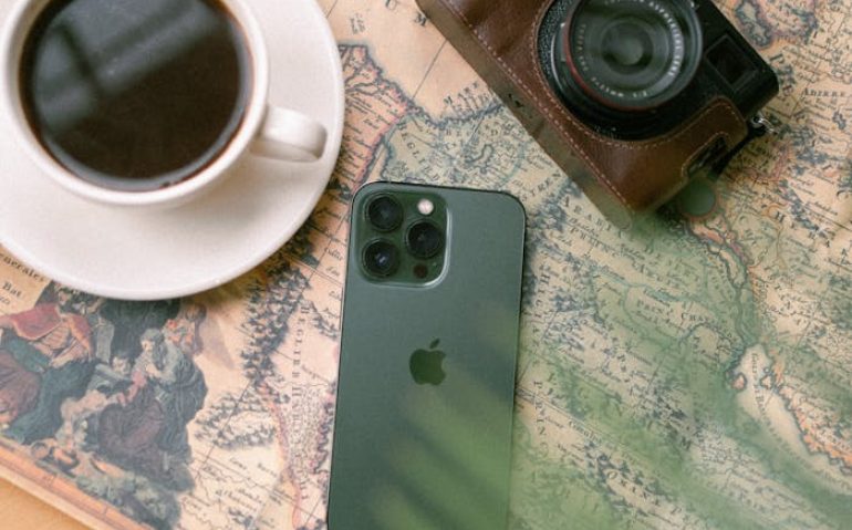 Flat lay of a coffee cup, vintage camera, and smartphone on a world map, evoking travel vibes.