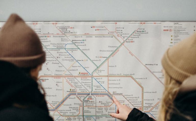Two people in warm clothing navigate a subway map on a station platform at night.