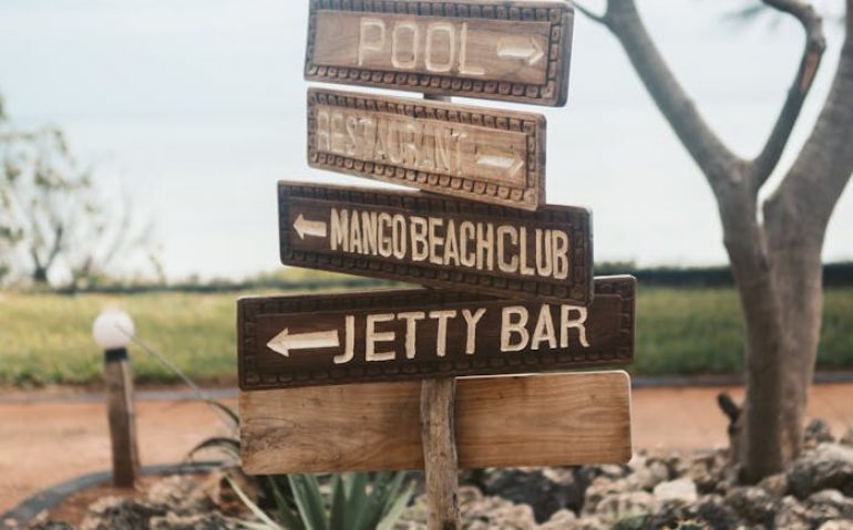 Rustic wooden signpost in a tropical setting pointing to pool, mango beach club, and jetty bar.
